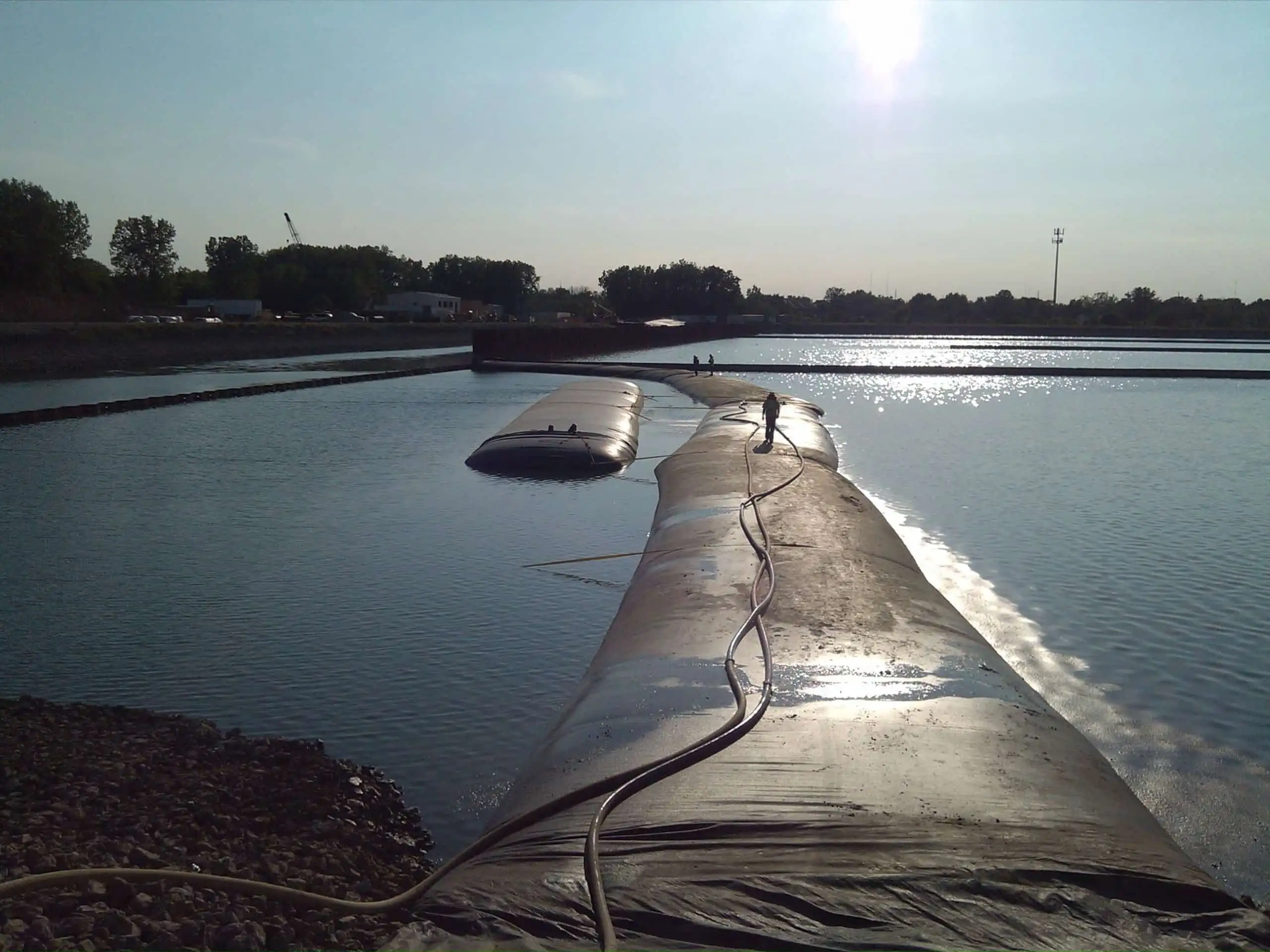 Crew walking a water-filled cofferdam stretched across open water at dusk